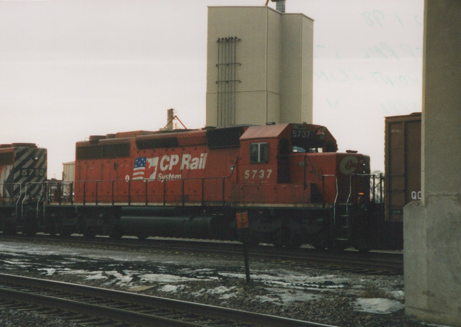 A red CP Rail System diesel locomotive, number 5737, stands on a track in a snowy yard, with another locomotive and a freight car visible in the background.