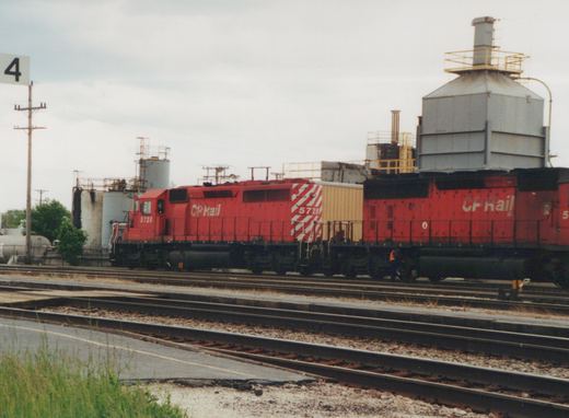 A red CP Rail diesel locomotive with the number 5728 is on a set of tracks, with a second red locomotive behind it, in an industrial yard setting.