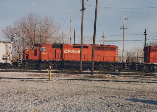 A red Canadian Pacific diesel locomotive, numbered 5703, sits on tracks in a snowy yard with another locomotive behind it.