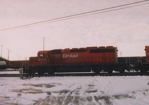 A red Canadian Pacific GP9 diesel locomotive, number 5722, is parked on a snowy railroad track, with another locomotive and freight cars visible behind it.