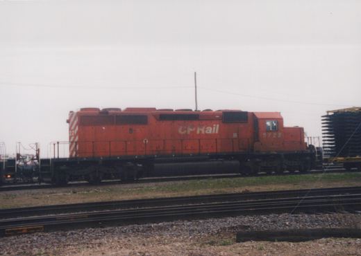 A red Canadian Pacific diesel locomotive, number 5722, is parked on tracks in a gravel yard under an overcast sky.