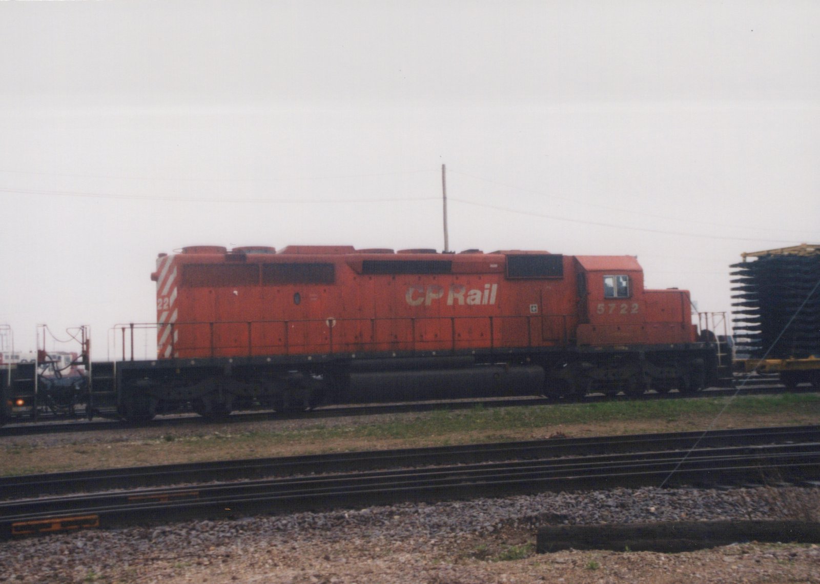 A red Canadian Pacific diesel locomotive, number 5722, is parked on tracks in a gravel yard under an overcast sky.