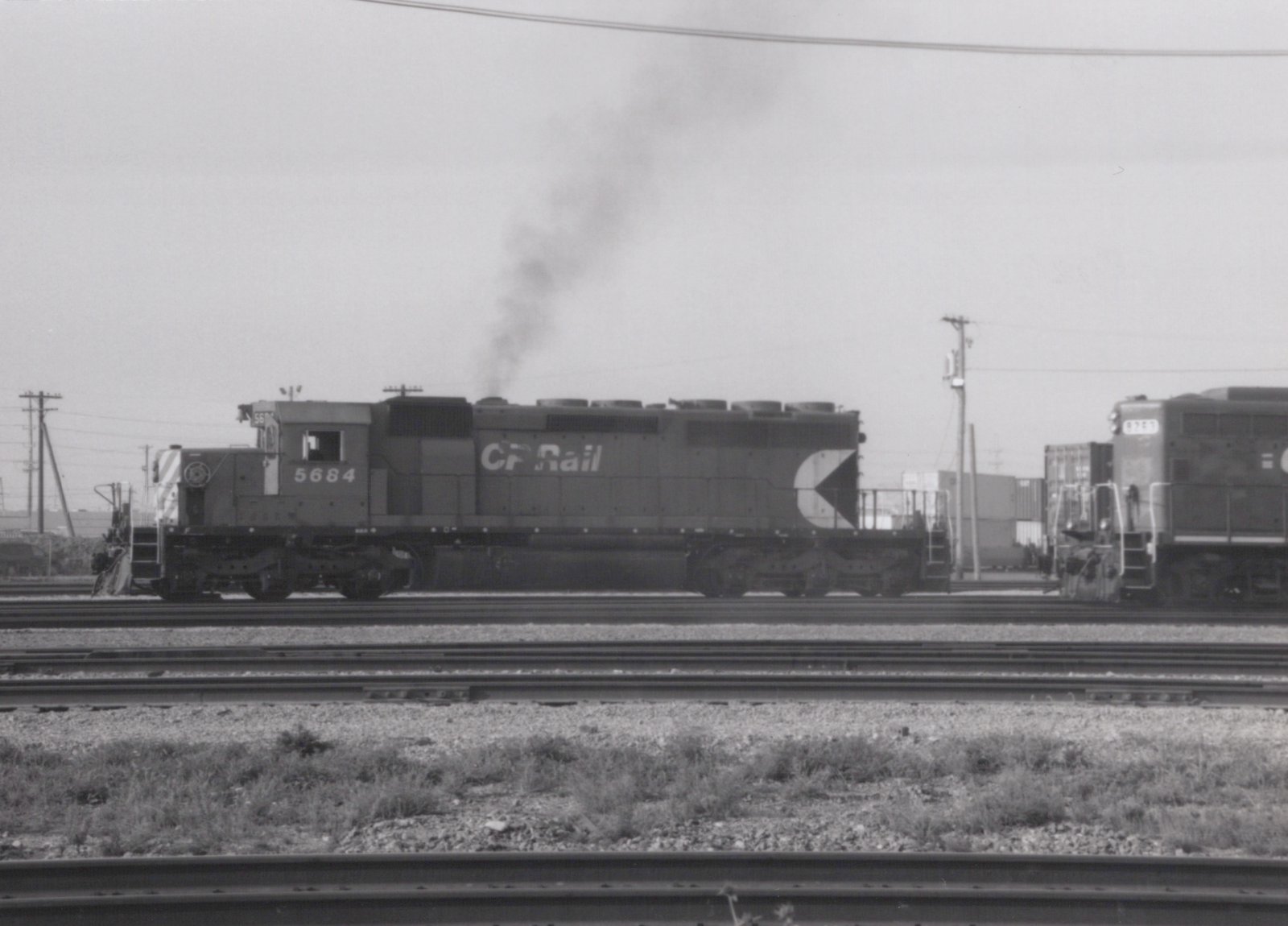 A black and white photo of a Canadian Pacific diesel locomotive, number 5684, on multiple tracks at a rail yard with smoke rising from its stack.