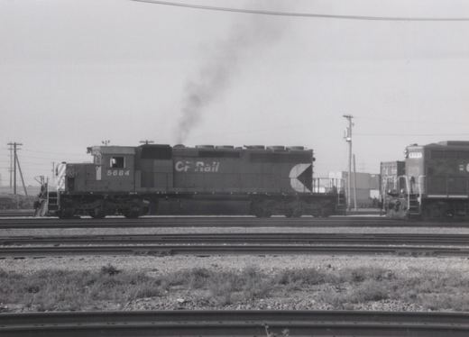 A black and white photo of a Canadian Pacific diesel locomotive, number 5684, on multiple tracks at a rail yard with smoke rising from its stack.