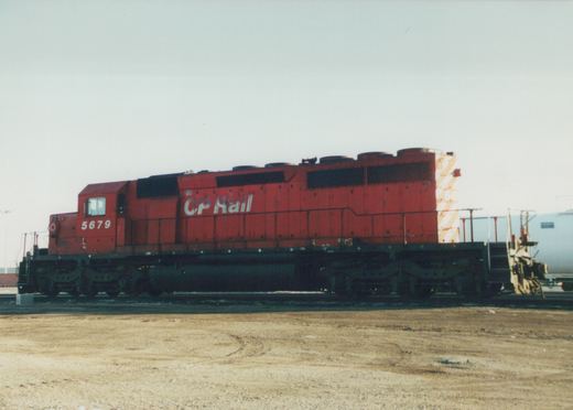 A side view of a red diesel locomotive with 'CP Rail' and the number '5679' on its side, standing on tracks in a gravel yard under a gray sky.