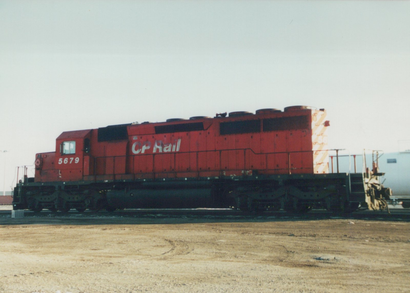 A side view of a red diesel locomotive with 'CP Rail' and the number '5679' on its side, standing on tracks in a gravel yard under a gray sky.