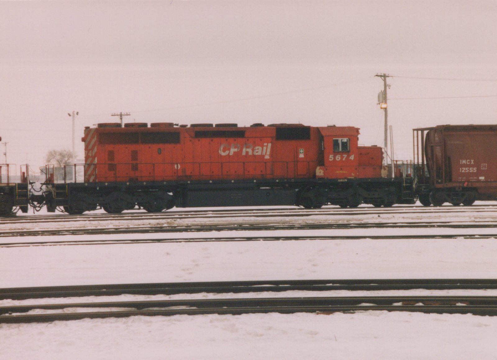 A red CP Rail diesel locomotive with the number 5674 is parked on tracks in a snowy yard, with a freight car visible to its right.