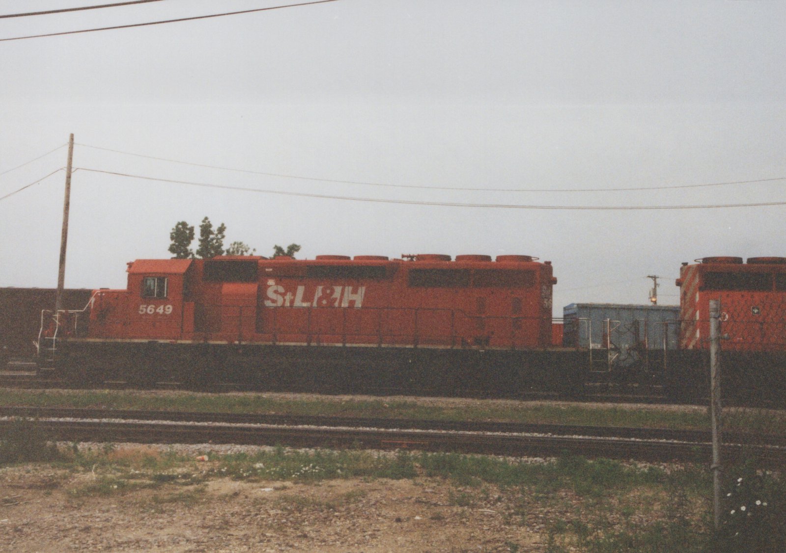 Side view of an orange St. Louis and Hannibal Railroad diesel locomotive number 5649 on a railroad track under an overcast sky.