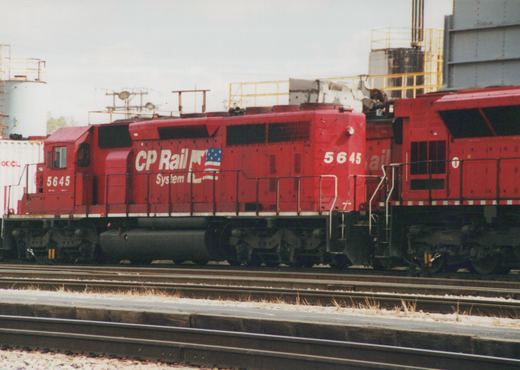 A red CP Rail System diesel locomotive, number 5645, sits on tracks in a rail yard, with a partial view of a second unit behind it.