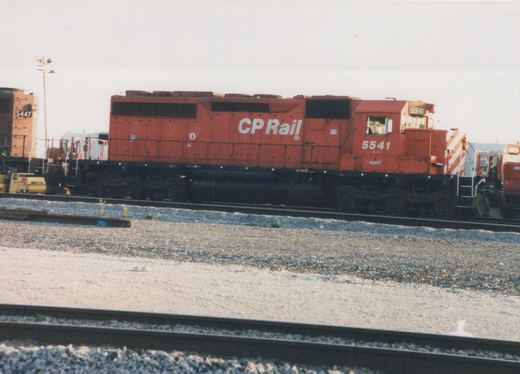 Side view of a red Canadian Pacific diesel locomotive numbered 5541 parked in a gravel yard with another locomotive in the background.