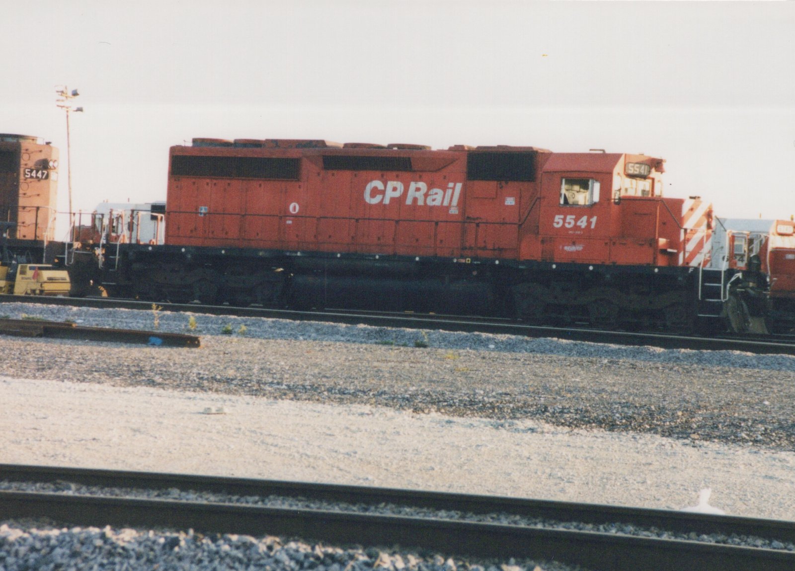 Side view of a red Canadian Pacific diesel locomotive numbered 5541 parked in a gravel yard with another locomotive in the background.