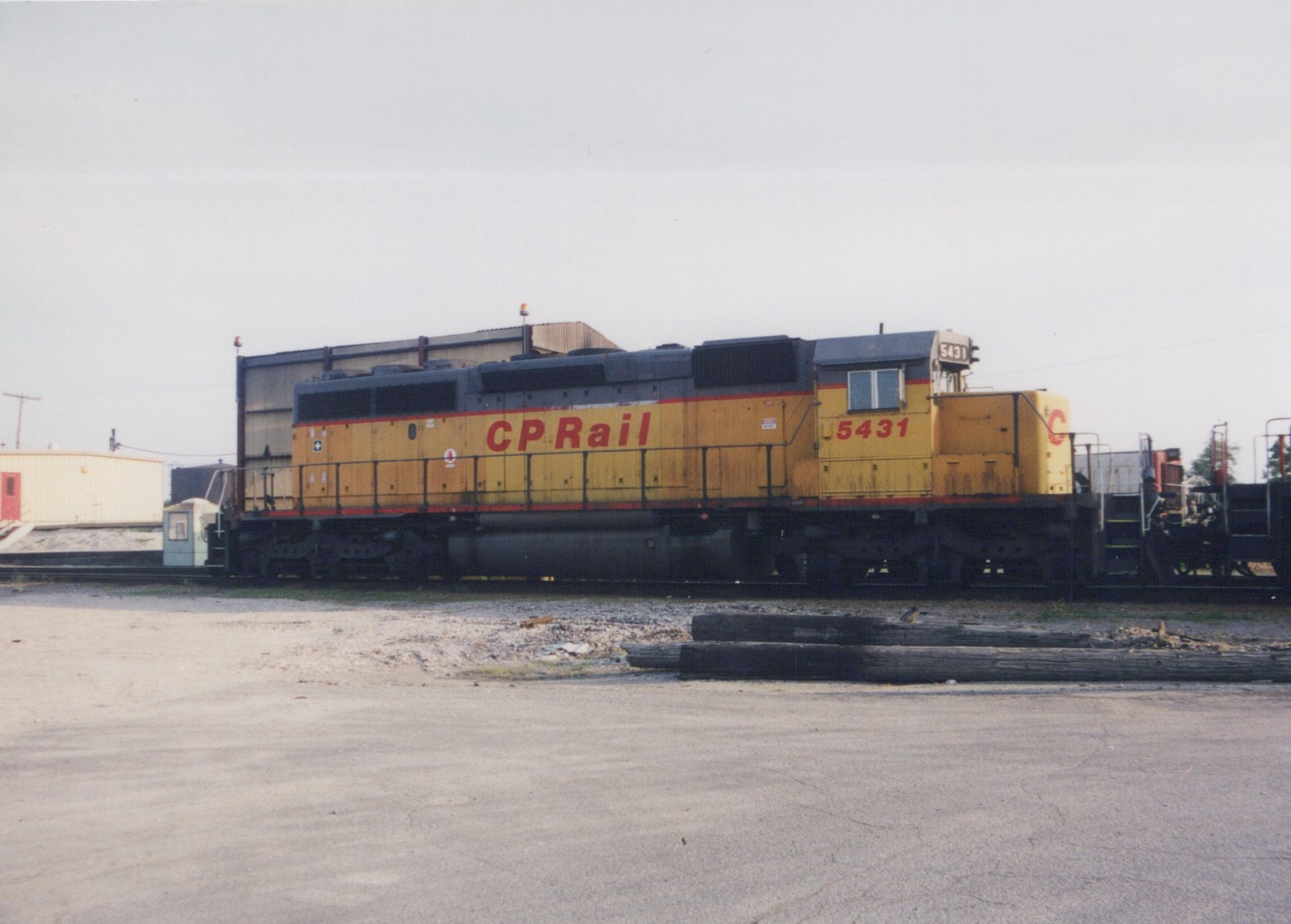 A yellow and red Canadian Pacific locomotive numbered 5431 is parked on a track in a rail yard under an overcast sky.