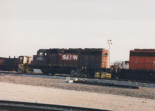 A St. Louis and Hannibal Railroad diesel locomotive numbered 5447 is parked in a rail yard with other equipment nearby.