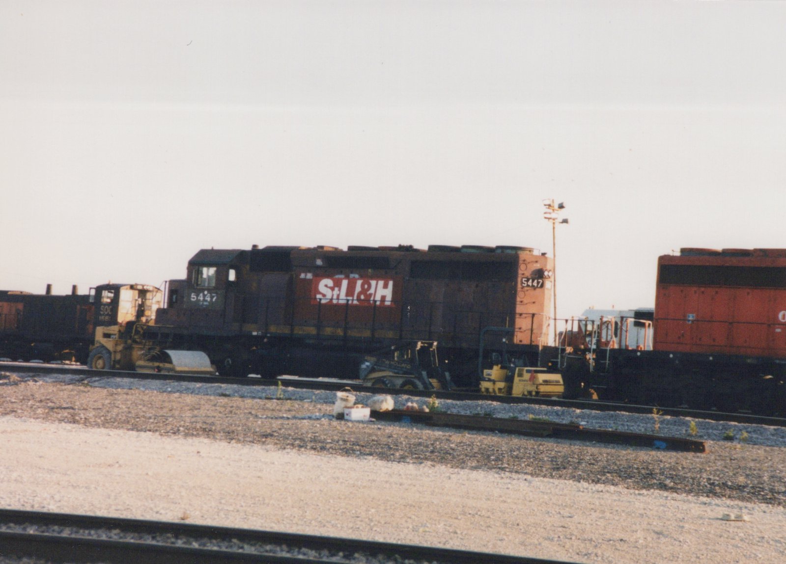 A St. Louis and Hannibal Railroad diesel locomotive numbered 5447 is parked in a rail yard with other equipment nearby.
