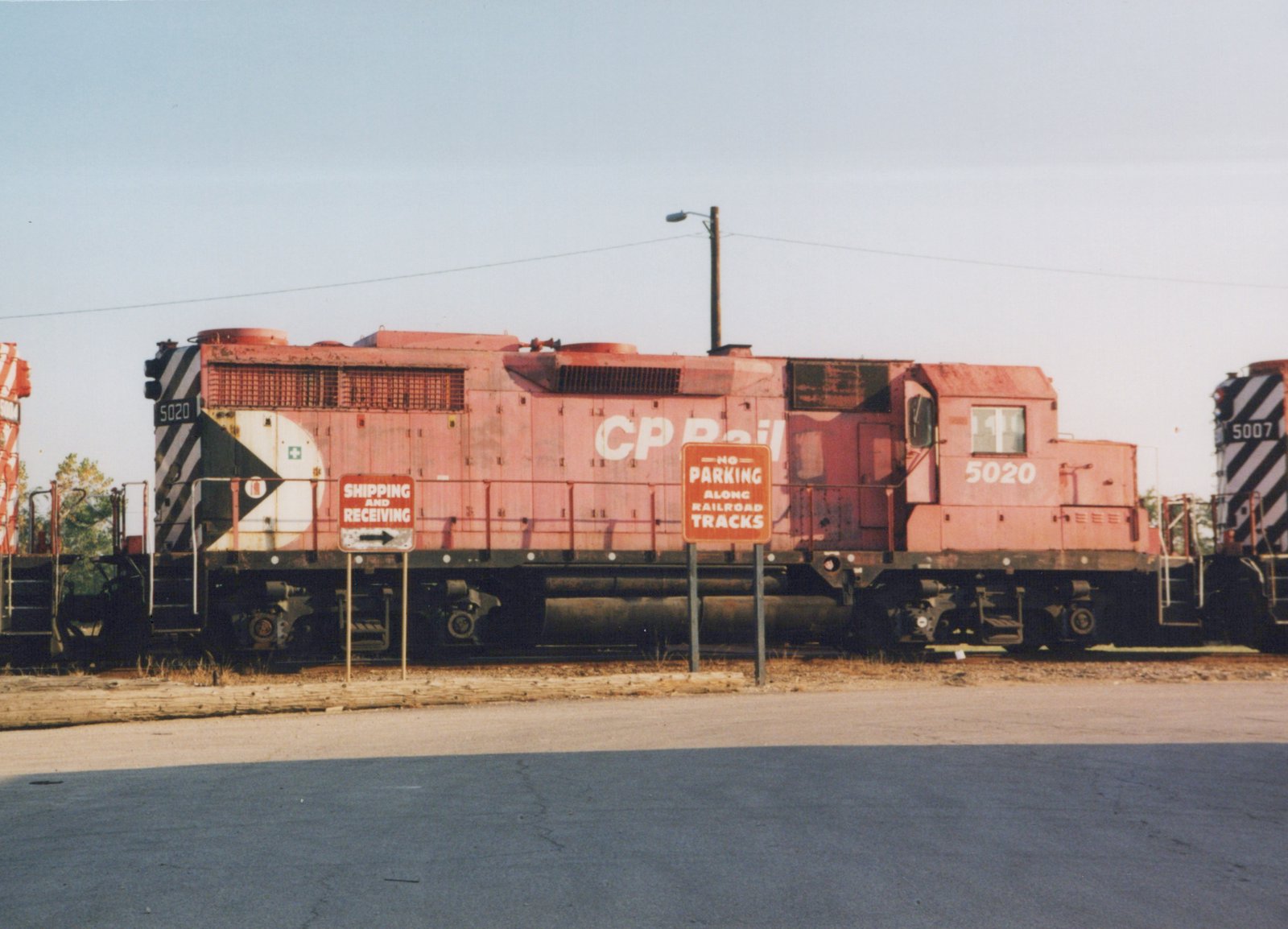A red Canadian Pacific locomotive numbered 5020 is parked in a yard, viewed from the side, with signs indicating no parking along the railroad tracks.