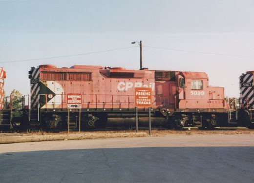 A red Canadian Pacific locomotive numbered 5020 is parked in a yard, viewed from the side, with signs indicating no parking along the railroad tracks.