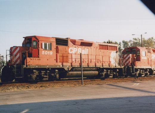 A side view of two red Canadian Pacific locomotives, numbered 5019 and 5008, parked on parallel tracks in a sunny yard.