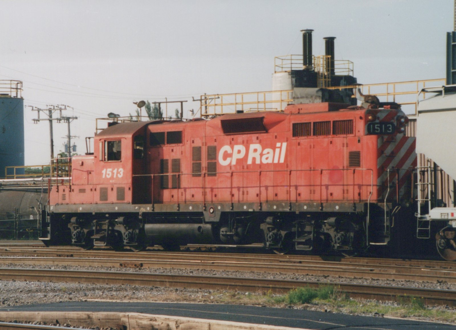 A bright red Canadian Pacific locomotive numbered 1513 is shown on railroad tracks, with industrial structures in the background.