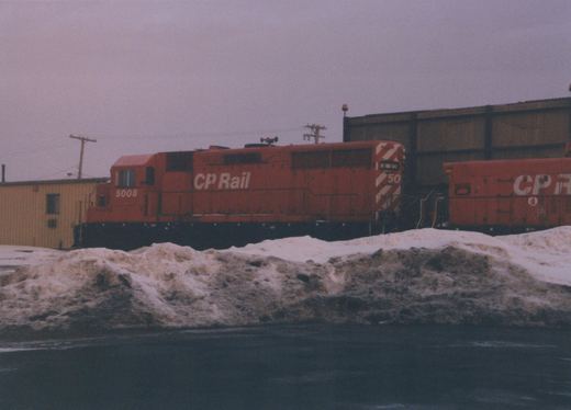 A red Canadian Pacific diesel locomotive numbered 5008 is parked in a snowy yard, with another red CP locomotive partially visible beside it.