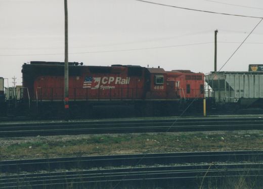 A red CP Rail System diesel locomotive, number 4618, is shown in profile on a railroad track next to a gray GATX freight car in a yard under an overcast sky.