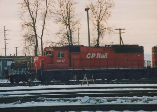 A red CP Rail diesel locomotive numbered 4617 is parked on multiple snow-covered tracks in a rail yard on an overcast winter day.