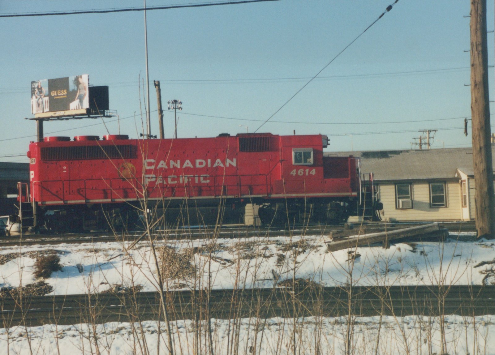 A red Canadian Pacific locomotive numbered 4614 is parked on snow-covered tracks with a GUESS billboard in the background.