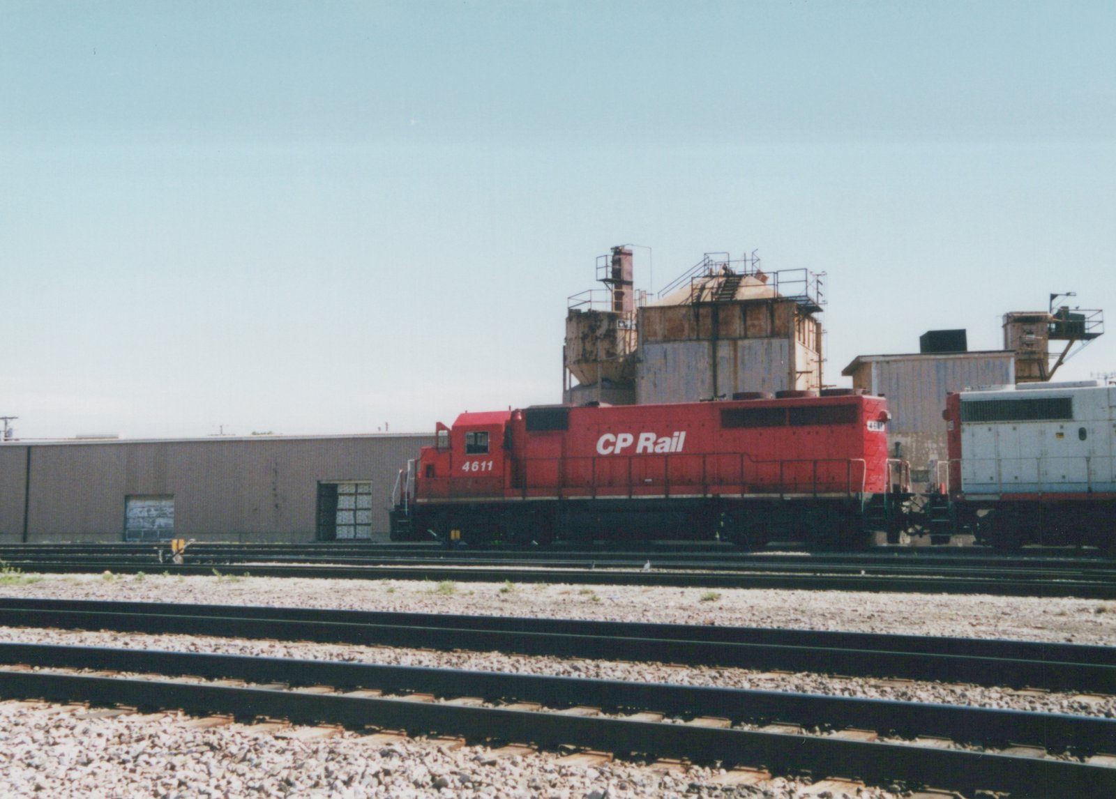 A red Canadian Pacific locomotive numbered 4611 sits on railroad tracks in a yard, with industrial buildings in the background.
