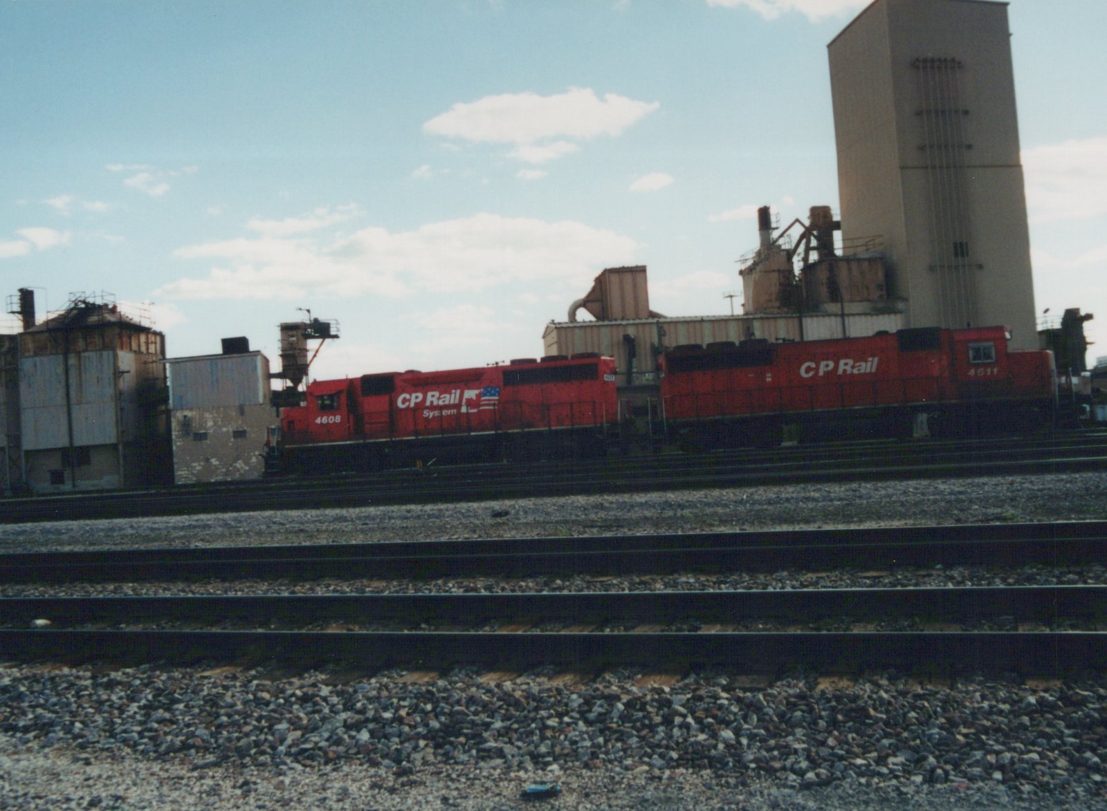 Side view of two red CP Rail System diesel locomotives on tracks in front of an industrial building on a clear day.