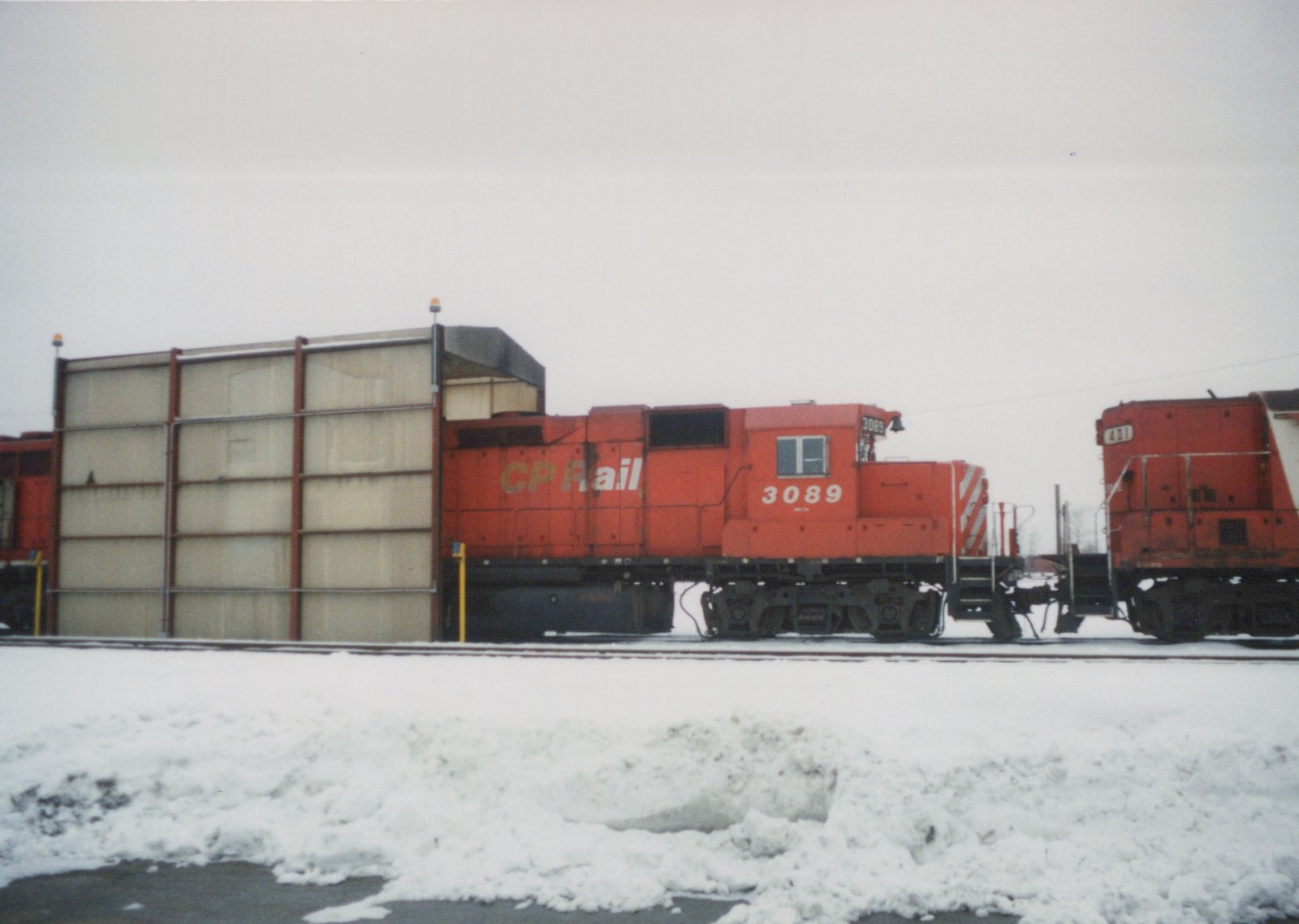 Two Canadian Pacific diesel locomotives, numbers 3089 and 401, are parked side by side on a snow-covered rail yard under an overcast sky.