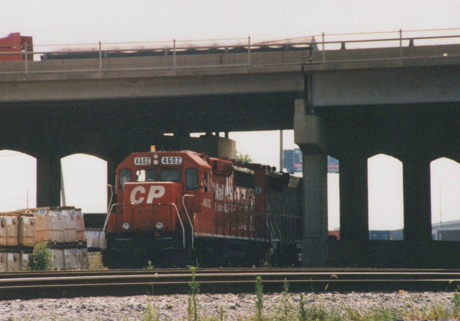 A red Canadian Pacific diesel locomotive numbered 4602 moves on tracks beneath a large concrete bridge on a cloudy day.