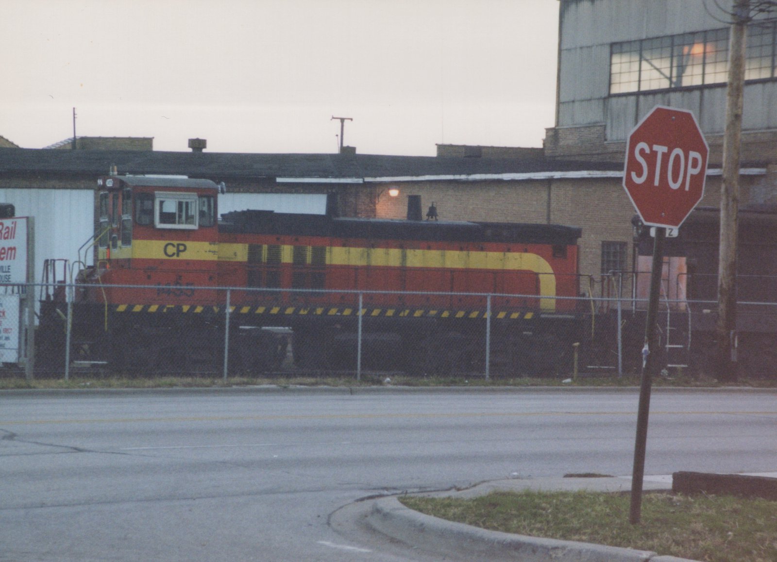 A side view of a Canadian Pacific diesel locomotive, number 1435, in red and yellow livery, behind a fence with a stop sign in the foreground.