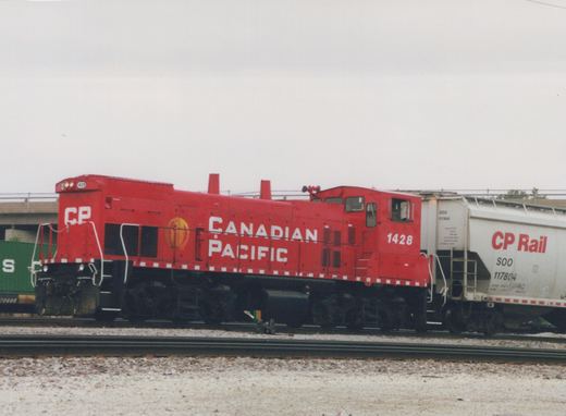 A red Canadian Pacific locomotive number 1428 pulling white and green freight cars on a set of tracks with a concrete overpass in the background under a cloudy sky.