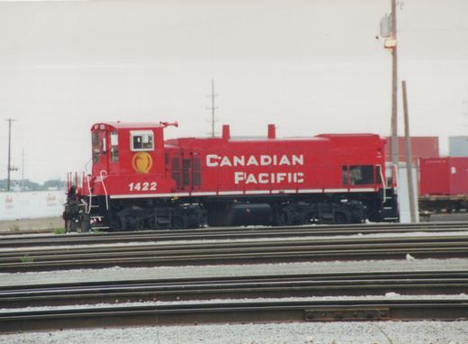 A red Canadian Pacific diesel locomotive numbered 1422 sits on multiple tracks in a rail yard under an overcast sky.