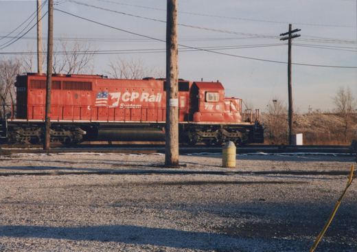 A red diesel locomotive with the number 778 and 'CP Rail System' lettering is parked in a gravel yard with bare trees and power poles, under a clear winter sky.