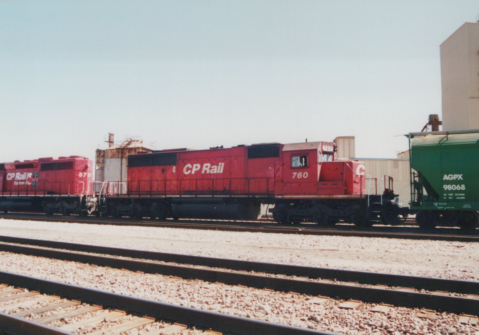 Two red CP Rail diesel locomotives numbered 760 and 5757 are parked on parallel tracks in a rail yard, with a green AGPX freight car visible to the right.