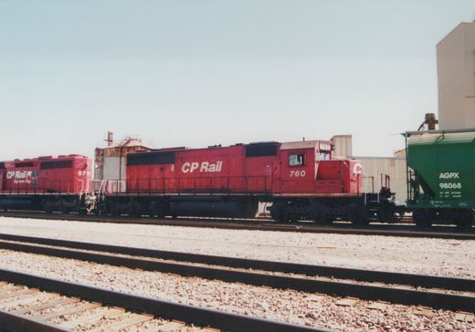 Two red CP Rail diesel locomotives numbered 760 and 5757 are parked on parallel tracks in a rail yard, with a green AGPX freight car visible to the right.
