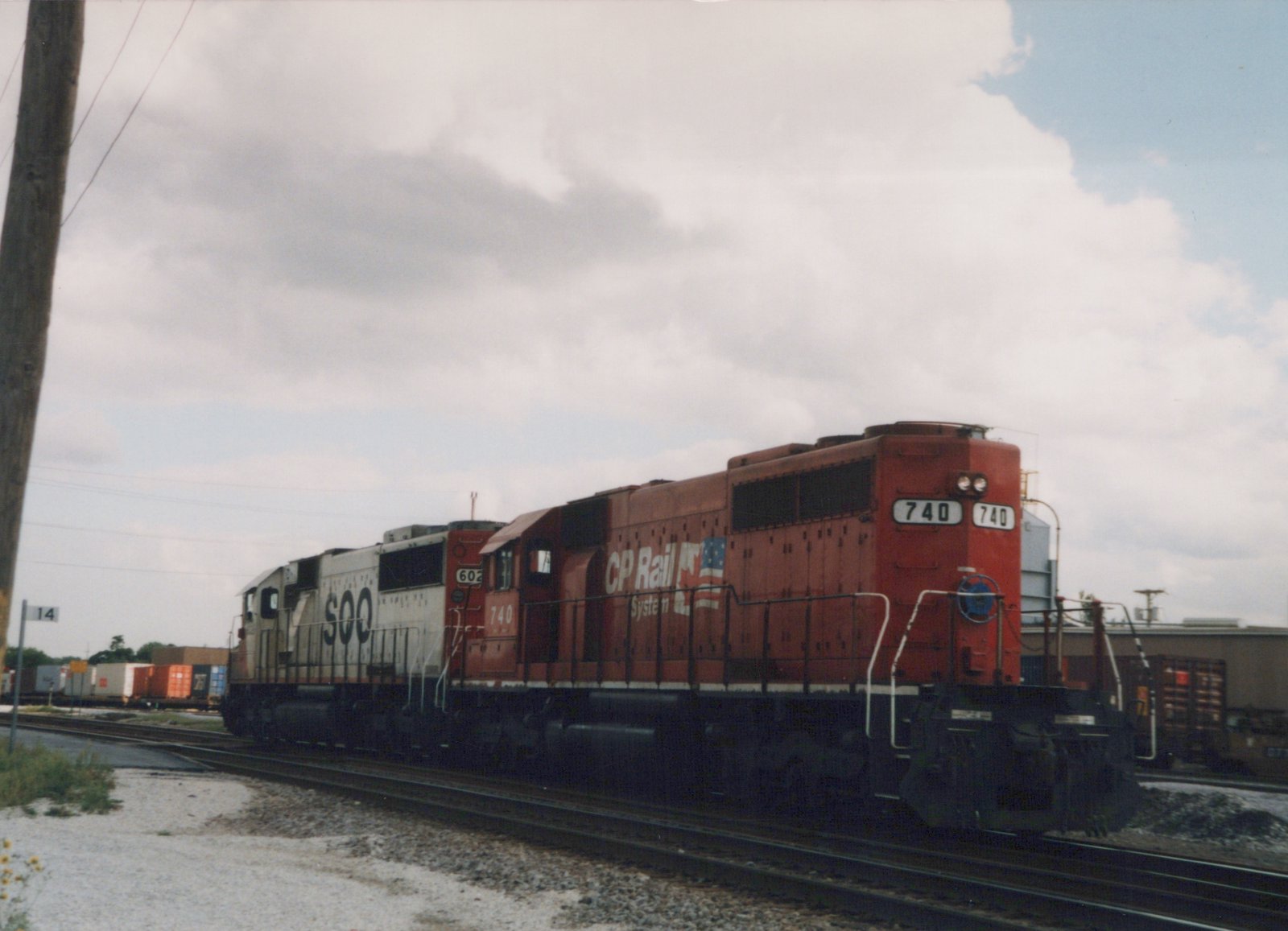 A red CP Rail System locomotive numbered 740 is in the foreground on a set of railroad tracks, with a white SOO Line locomotive numbered 602 behind it. The sky is overcast, and the setting appears to be a rail yard.