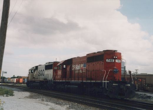 A red CP Rail System locomotive numbered 740 is in the foreground on a set of railroad tracks, with a white SOO Line locomotive numbered 602 behind it. The sky is overcast, and the setting appears to be a rail yard.