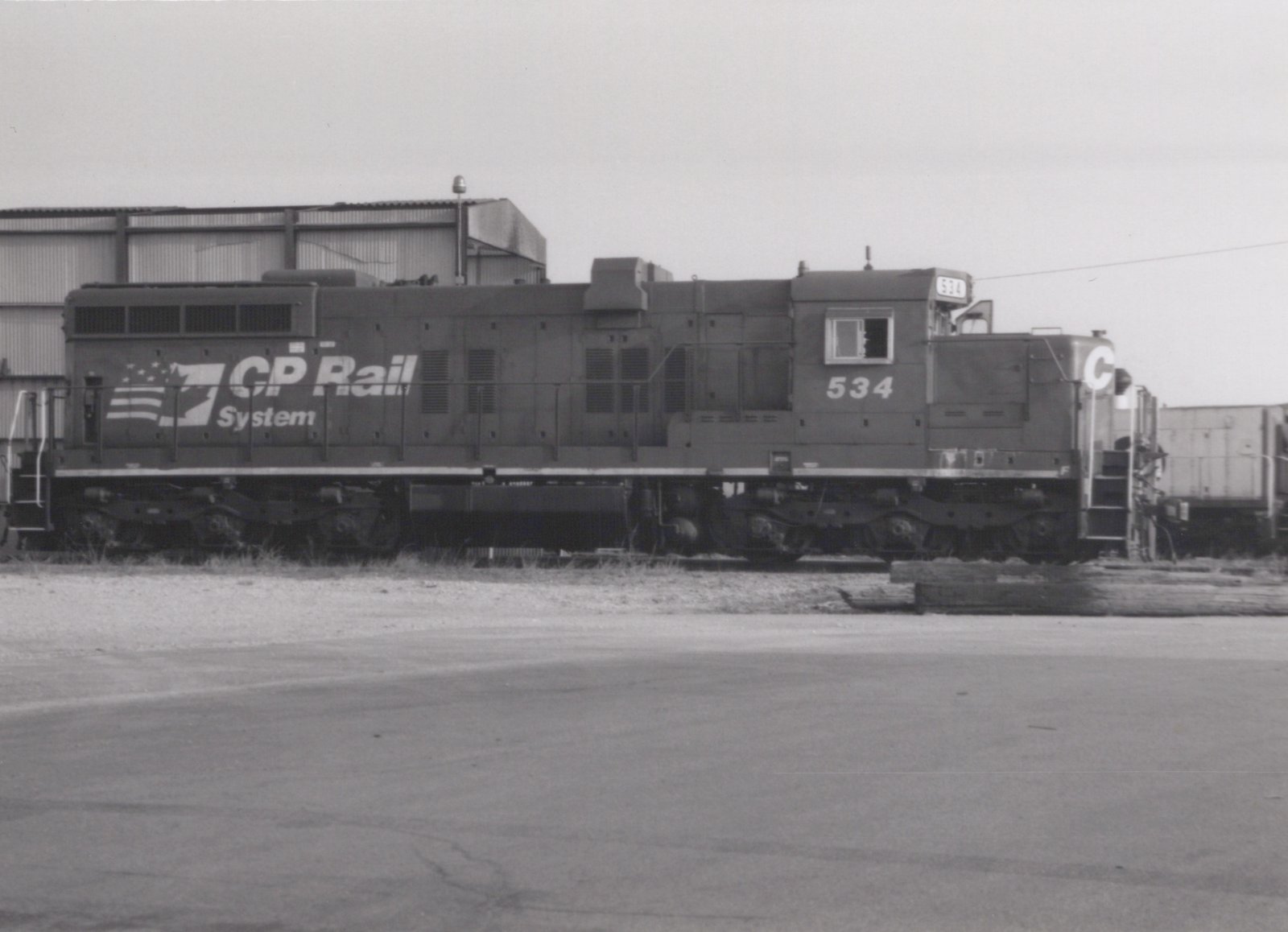 Side view of a CP Rail System diesel locomotive numbered 534 in a rail yard with industrial buildings in the background.