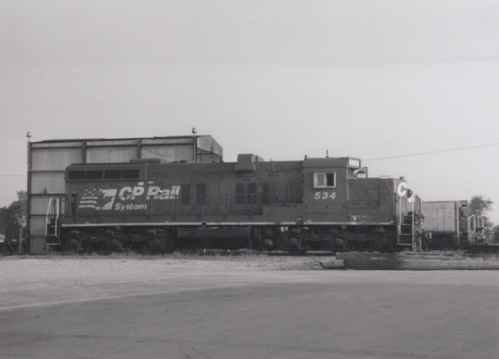 A black and white photograph of a CP Rail System diesel locomotive, number 534, standing in a railyard next to a building under an overcast sky.