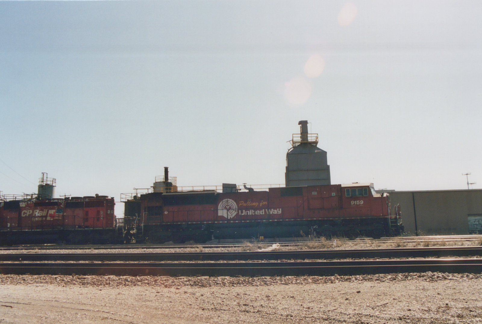 Two red Canadian Pacific diesel locomotives, numbered 56 and 9159, are parked in a railyard, the latter featuring a 'Pulling for United Way' logo on its side.
