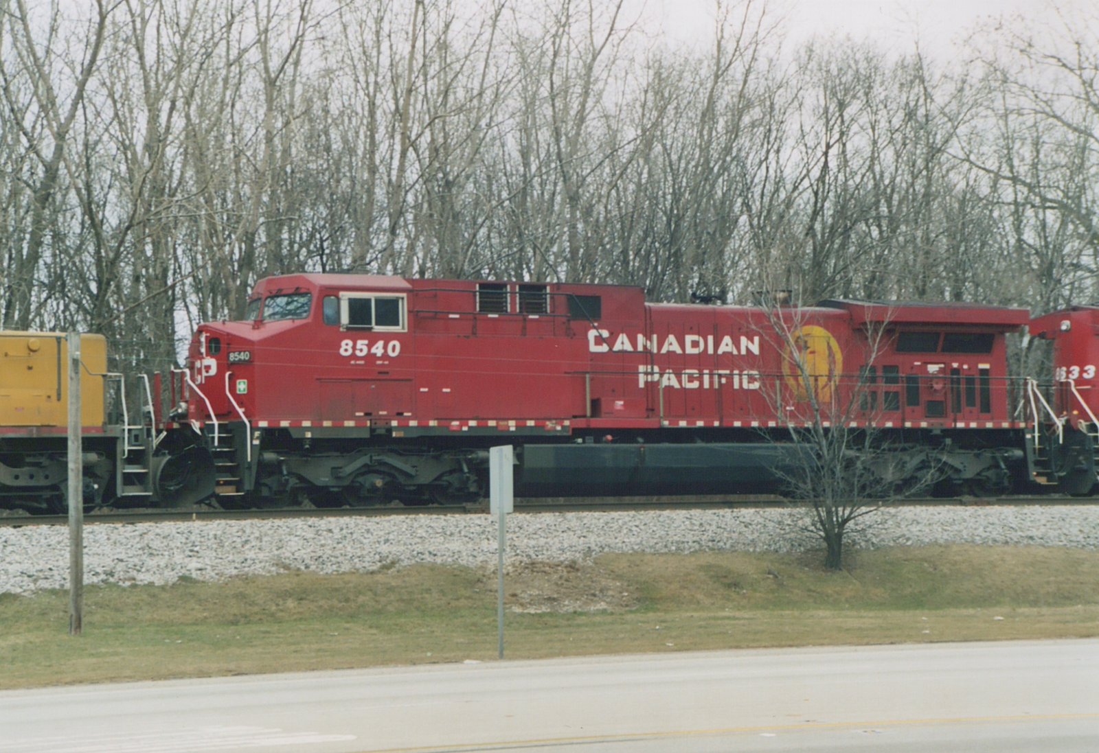A red Canadian Pacific diesel locomotive, numbered 8540, sits on a railway track beside a road with bare trees in the background.