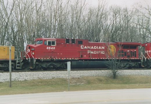 A red Canadian Pacific diesel locomotive, numbered 8540, sits on a railway track beside a road with bare trees in the background.