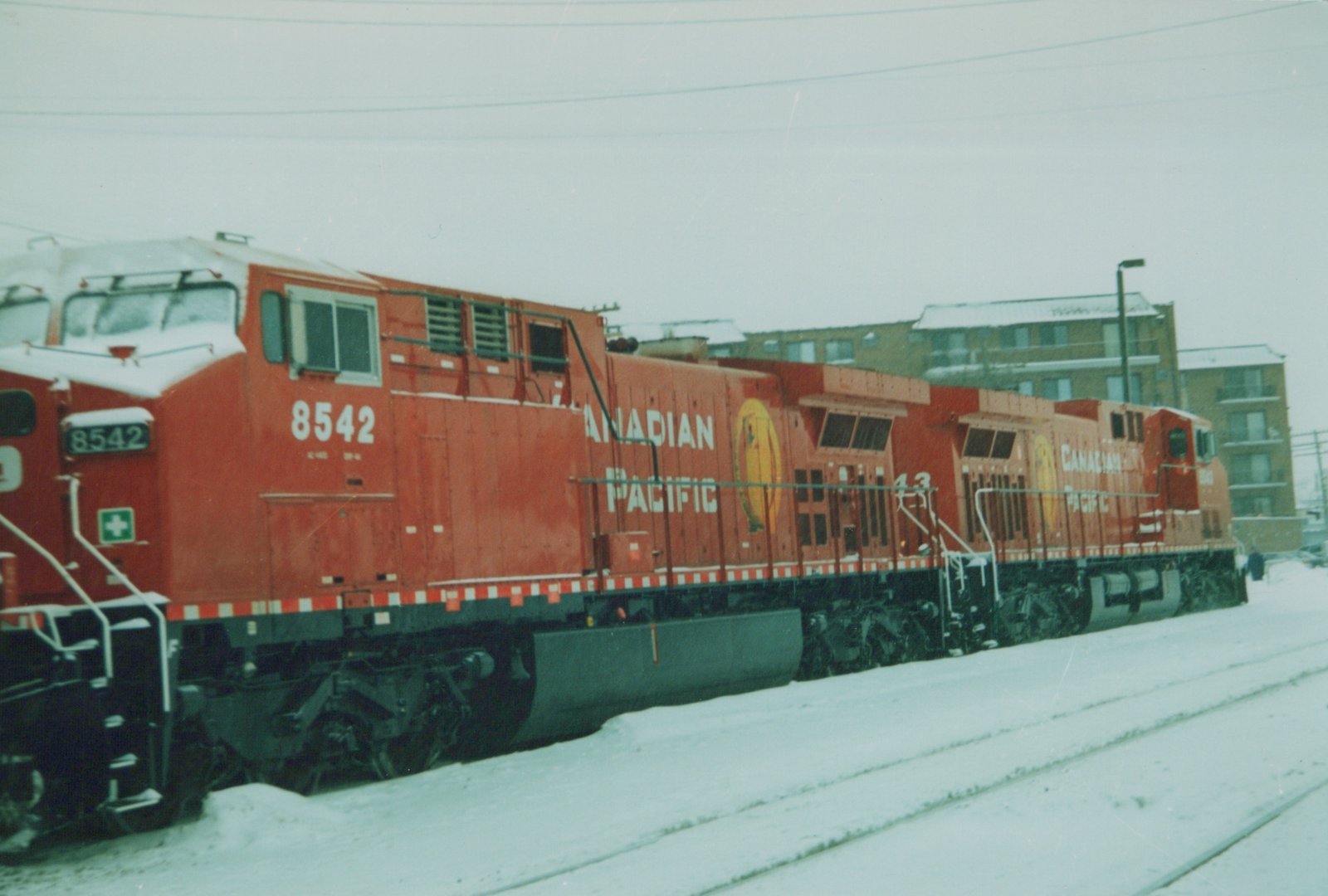 Two red Canadian Pacific diesel locomotives, numbers 8542 and 43, on snowy railroad tracks with buildings in the background.