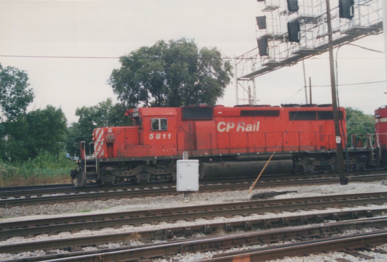 A red CP Rail diesel locomotive, number 5811, stands on a set of tracks in a rail yard with green trees in the background.