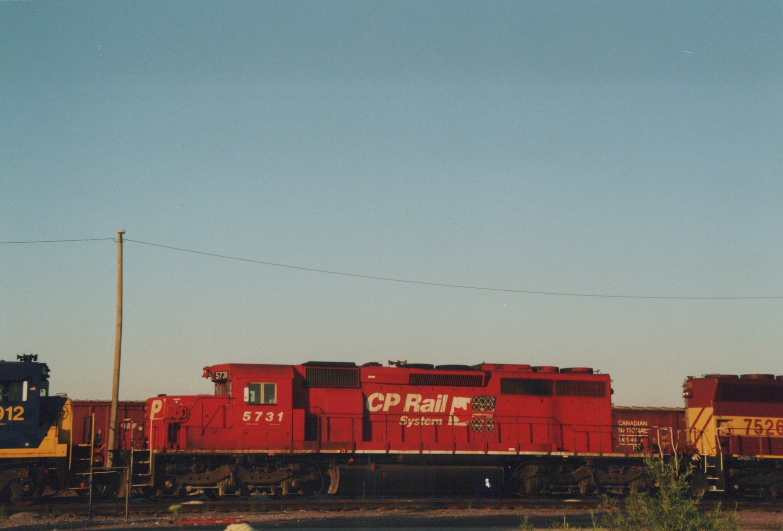 A side view of a red CP Rail System diesel locomotive, number 5731, in a rail yard with other locomotives and freight cars visible.