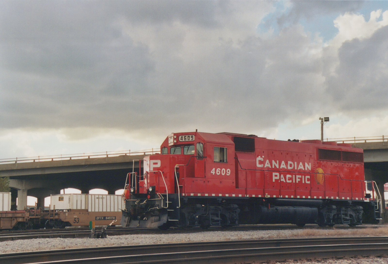 A red Canadian Pacific GP9 locomotive, numbered 4609, stands on a railroad track beneath a concrete overpass on a cloudy day.