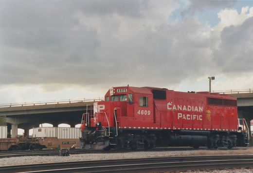 A red Canadian Pacific GP9 locomotive, numbered 4609, stands on a railroad track beneath a concrete overpass on a cloudy day.