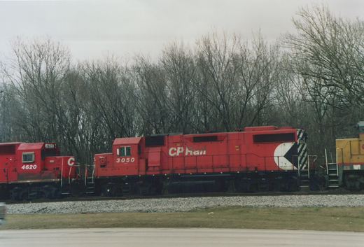 Three red and yellow Canadian Pacific diesel locomotives on a railroad track with bare trees in the background on an overcast day.