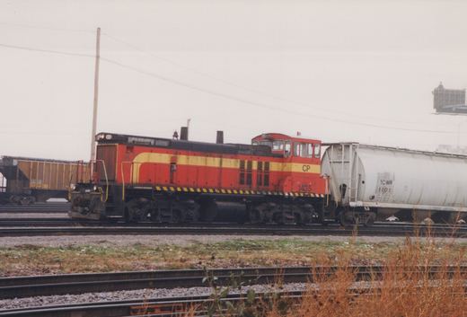 A red and yellow Canadian Pacific GP9 diesel locomotive, number 1435, is parked in a rail yard with a white TCWR tank car and a brown ON boxcar nearby.